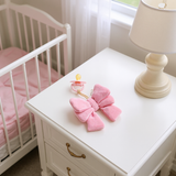 Pink butterfly toy and pacifier on a white nightstand next to a crib in a nursery.