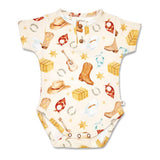 A short-sleeve baby bodysuit with a western-themed print on a cream background, featuring cowboy boots, hats, bandanas, horseshoes, stars, and lasso details.