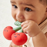 Baby holding a red and green teething toy with a smiley face design.