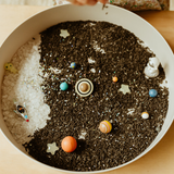 Sensory bin with materials resembling a solar system, including planets and stars.