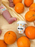 Baby's feet near oranges and a container labeled 'babió' on a yellow blanket