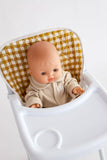 Baby doll in a high chair with a checkered cushion on a white background