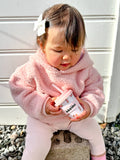 Child in pink outfit holding a container with a straw outdoors