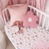A pink and white mermaid-themed crib sheet displayed in a white wooden baby crib, styled with a pink pillow, a flower-shaped cushion, and a plush bunny. A circular tag on the sheet reads 'SLEEP'.