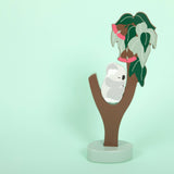 Decorative item with a white owl on a brown branch against a light green background