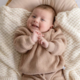 Baby in a beige knit outfit lying on a textured blanket
