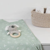 Knitted koala toy with a wooden ring on a green blanket next to a woven basket.