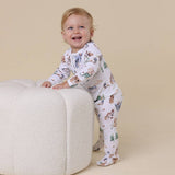Child wearing a patterned outfit sitting on a white cushion against a beige background