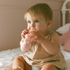 Baby holding a pink toy on a bed with a neutral background