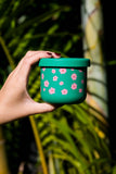 Hand holding a green container with pink floral pattern against a blurred natural background