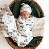 Newborn baby swaddled in a blanket with car patterns, wearing a matching hat, in a wicker basket.