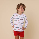 Child wearing a long-sleeve shirt with car prints and red shorts on a beige background