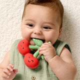 Baby holding a red and green teething toy with a neutral background