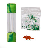 A clear cylindrical sensory tube with green textured caps, shown next to a clear bag filled with small green glitter pieces and a small orange dinosaur figure on a white background.