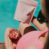 Person holding a glass of strawberries by a pool, with a package of Trujillo Kitchen product in the foreground.