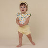 Child wearing a floral top and yellow shorts on a beige background