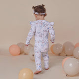 Child wearing a floral onesie surrounded by balloons on a beige background