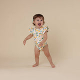 Child wearing a colorful onesie with a lemon pattern on a beige background