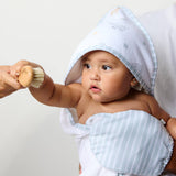 Baby wrapped in a towel with a hood, holding a wooden brush against a white background