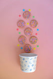 Sprinkled cookies arranged around a paper cup with a pink gradient background