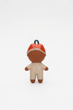 A small stylized doll figure with a brown body, cream-colored striped outfit, red hat, and a dark green loop at the top, centered on a plain white background.