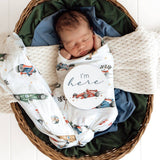 Newborn baby swaddled in a blanket with car patterns, lying in a woven basket.