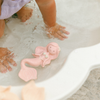 Pink mermaid bath toy in a bathtub with child's feet playing.