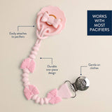 Pink pacifier clip with decorative bows and a clasp on a beige background