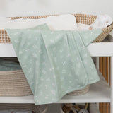 Green baby blanket with white patterns draped over a crib