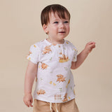 A toddler wearing a white short-sleeve top with a playful print of cartoon sheep and small green leaves, paired with beige shorts, set against a solid beige background.