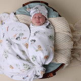 Newborn baby swaddled in a floral blanket with a 'I'm here' sign, lying in a wooden basket.