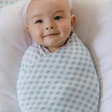 Baby swaddled in a blue and white checkered blanket on a white pillow