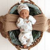 Newborn baby in a basket with animal print clothing and hat, surrounded by soft textures.