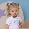 Young child with pigtails wearing a white shirt with shark designs in a room with a star-shaped object.