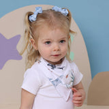 Young child with pigtails wearing a white shirt with shark designs in a room with a star-shaped object.