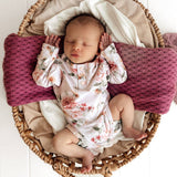 Newborn baby in a floral outfit lying in a woven basket with pink pillows.