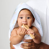 Baby holding a wooden toy with a white towel draped over its head