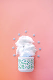 White cup with green pattern filled with fluffy white substance on a pink background