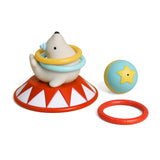 A children's toy set featuring a white polar bear sitting on a red and white circus-style base, with a yellow and light blue hula hoop around its neck. A light blue ball with a yellow star and a separate red ring are placed beside it on a clean white background.