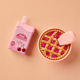 Pink cherry juice bottle and pie container with a pie on a peach background