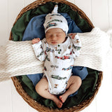 Newborn baby in a car seat with a patterned outfit and hat, surrounded by green and blue blankets.
