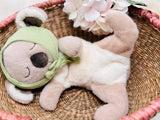 Plush toy resembling a bear with a green headband in a woven basket with flowers.