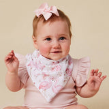 A baby wearing a pink ruffle-sleeve bodysuit and a white triangular bib printed with pink flamingos, posed against a solid beige background. The baby also wears a matching pink bow on her head.