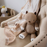 Knitted teddy bear on a beige chair with a basket of toys in the background