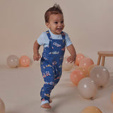 Child in blue patterned overalls standing among balloons on a beige background