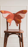 Butterfly-shaped cushion on a wooden chair against a white wall