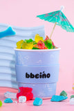 Stackable blue containers with gummy bears and a small umbrella on a pink background