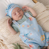A sleeping newborn baby wearing a light blue printed overall romper and matching beanie hat, resting on a cream knit blanket.