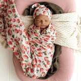 Newborn baby swaddled in a strawberry-patterned blanket on a pink surface