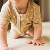 Baby in a beige outfit with shell pattern crawling on a soft surface